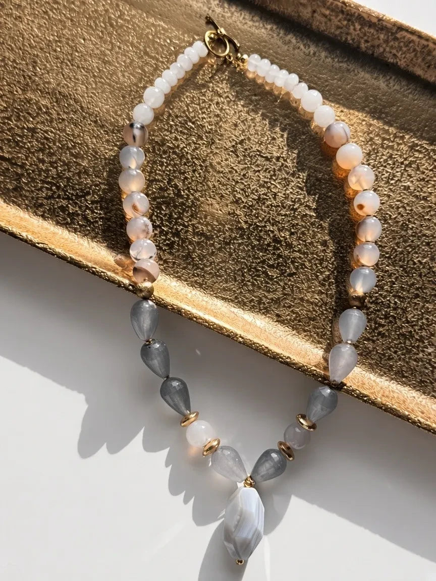 Hue La La Gems beaded necklace with blush, white, and grey agate stones and gold-tone spacers on a gold tray.