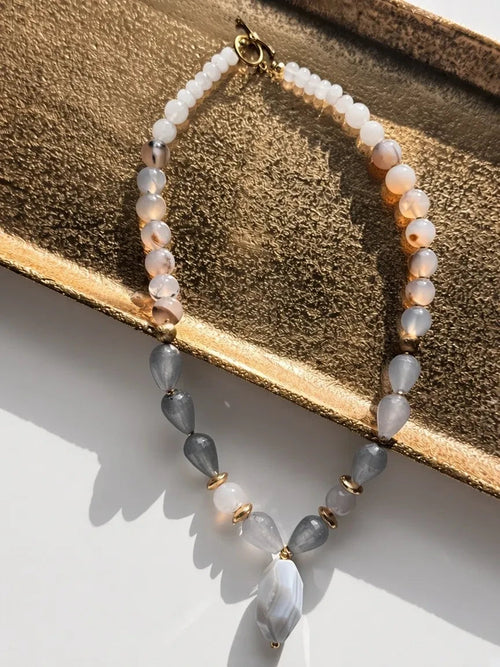 Hue La La Gems beaded necklace with blush, white, and grey agate stones and gold-tone spacers on a gold tray.