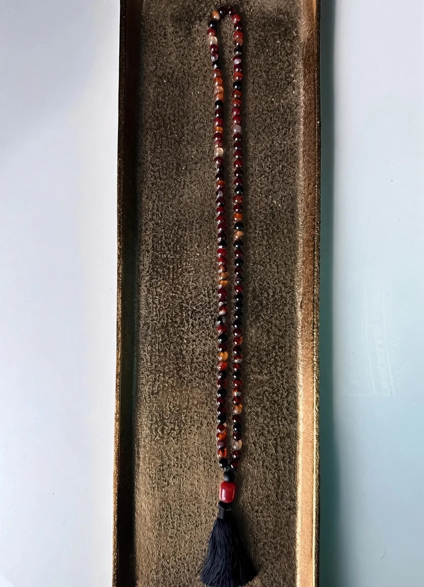 Hue La La Gems mala necklace with natural agate beads in red and brown tones, featuring a black silk tassel.