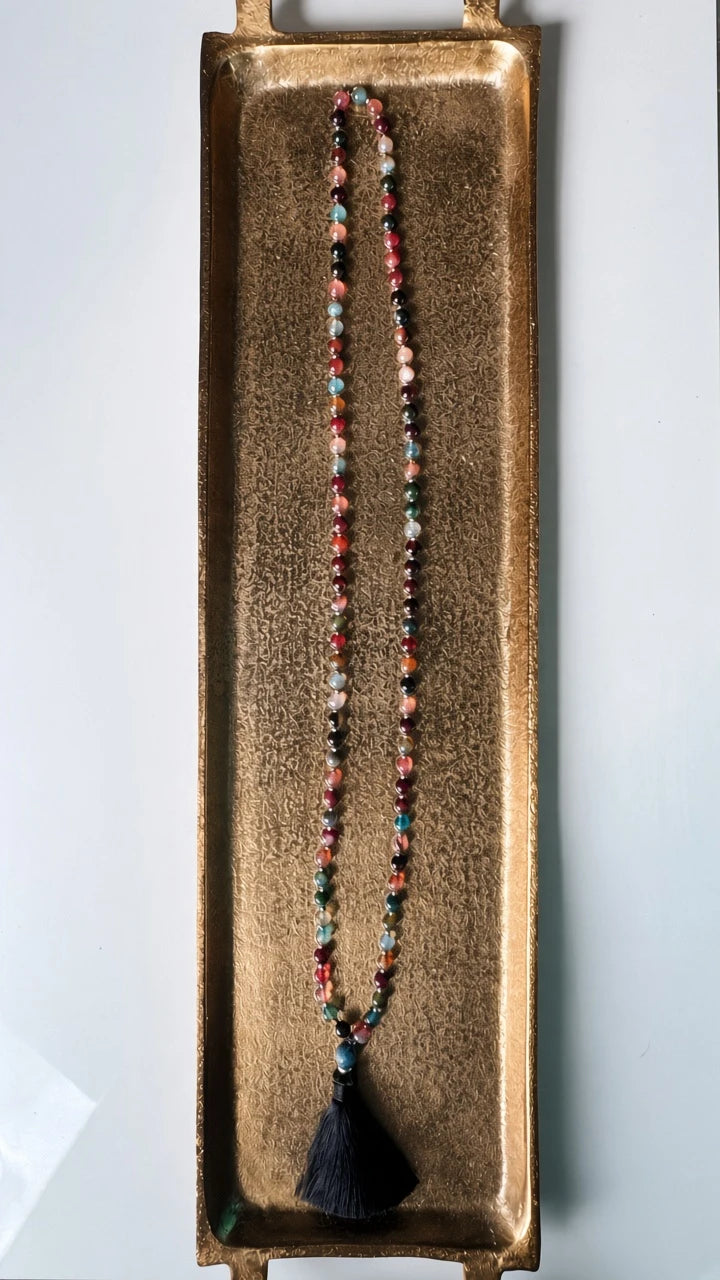 Hue La La Gems multi-colored agate mala necklace with silver spacers and a black silk tassel on a gold tray.