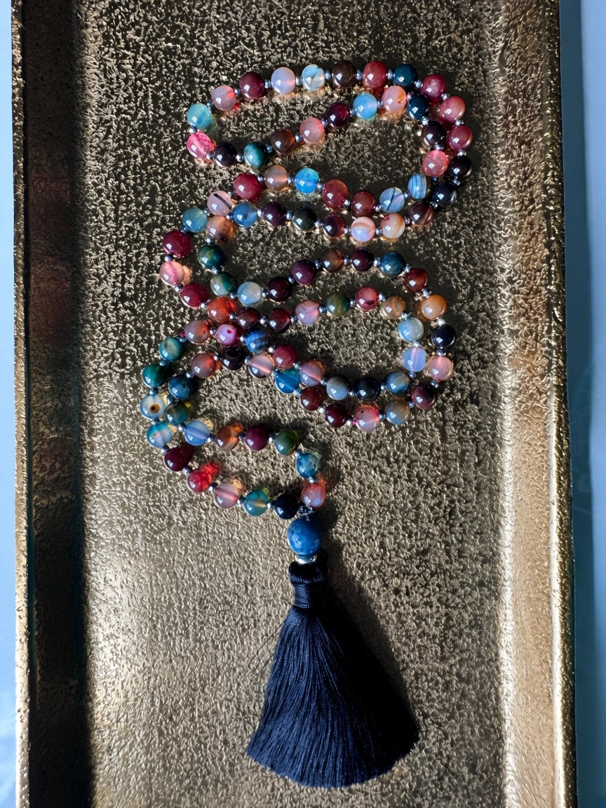 Hue La La Gems multi-colored agate mala necklace with silver spacers and a black silk tassel on a gold tray.