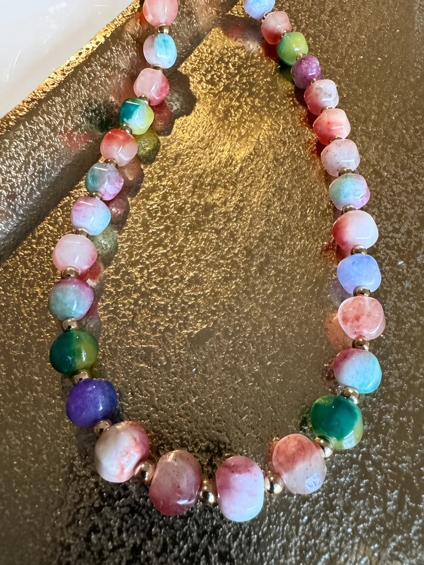 Hue La La Gems multi-colored gemstone beaded necklace with gold-tone spacers on a reflective gold surface.