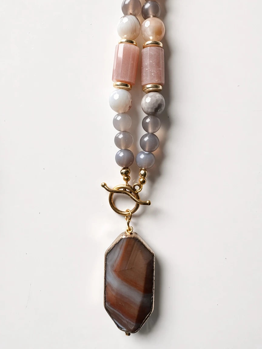 Hue La La Gems beaded necklace featuring grey agate, pink beads, and a gold-rimmed brown gemstone pendant with toggle.