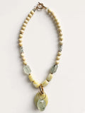Hue La La Gems handcrafted beaded statement necklace with cream beads, green gemstone drops, and yellow oval pendant.