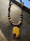 Hue La La Gems beaded statement necklace with burgundy, mustard, and peach gemstones and a geometric yellow pendant.