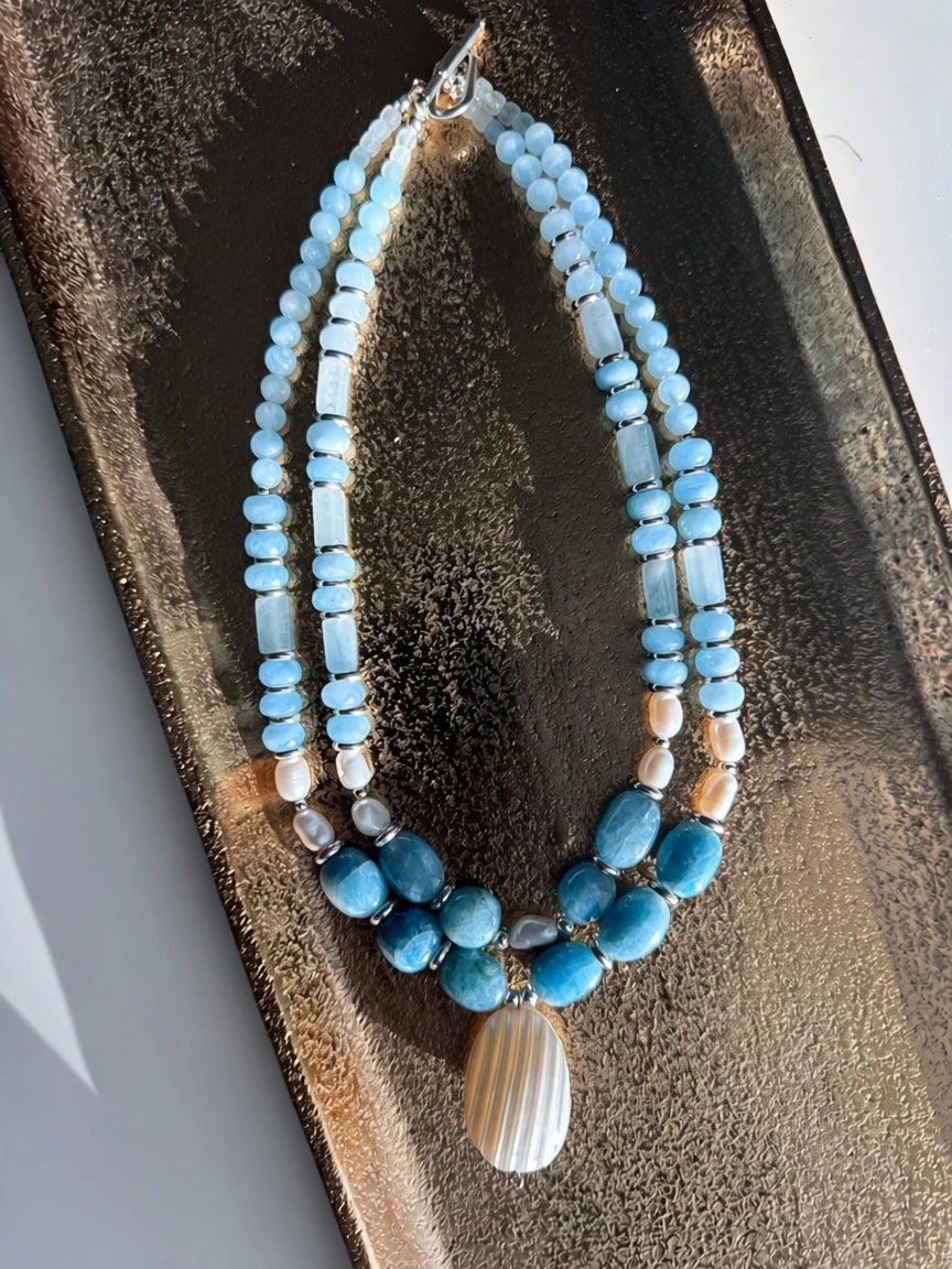 Hue La La Gems multi-strand statement necklace with blue aquamarine beads, freshwater pearls, and a shell pendant.