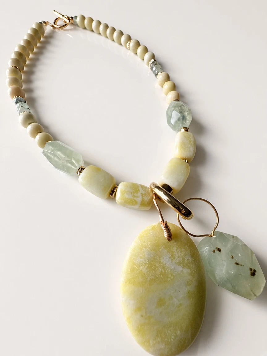 Hue La La Gems handcrafted statement necklace with cream beads, green gemstone drops, and a marbled yellow pendant.