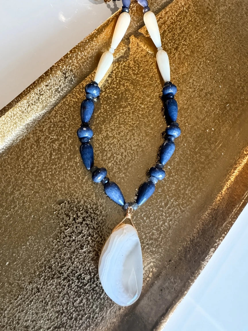Hue La La Gems artisan beaded necklace featuring navy blue stone beads, cream accents, and a gold-wrapped stone pendant.