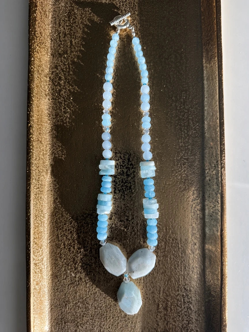 Hue La La Gems handcrafted statement necklace featuring blue aquamarine gemstones and clear crystal spacers on a tray.