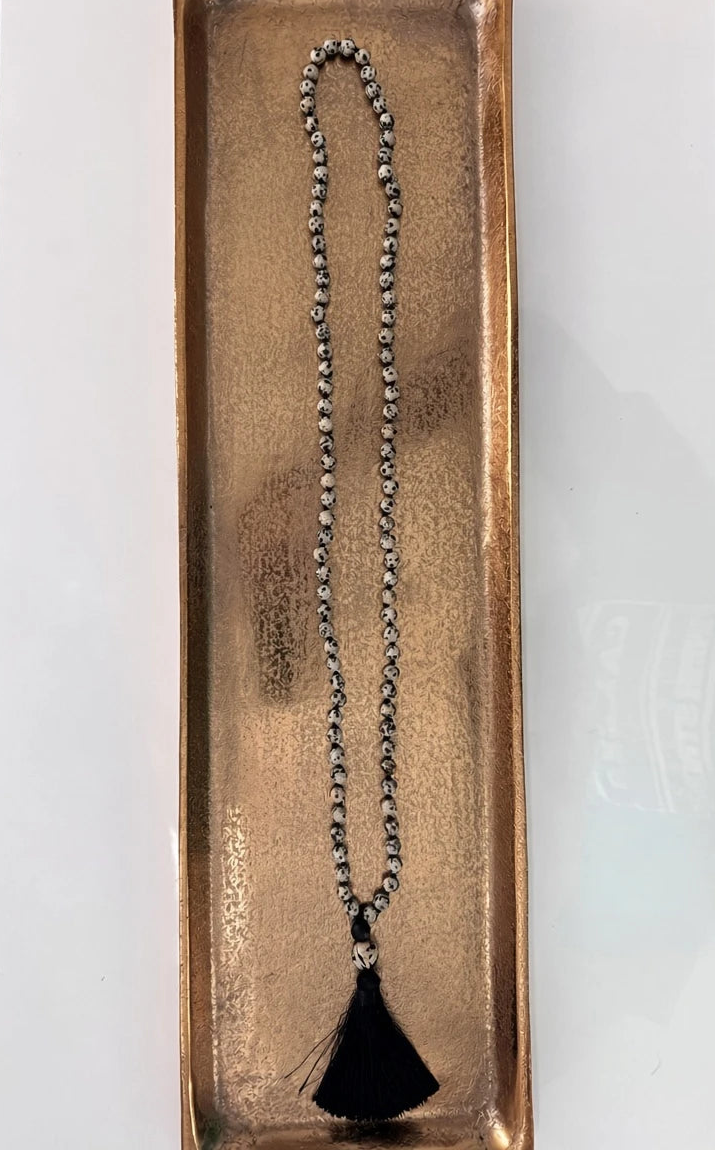 Hue La La Gems Dalmatian Jasper mala necklace with 108 hand-knotted beads and a black silk tassel on a gold tray.