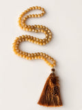 Hue La La Gems honey-toned gemstone beaded necklace with a brown feather tassel on a white background