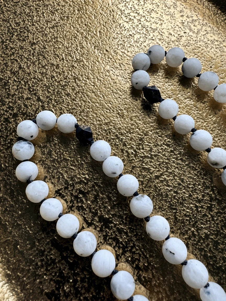 Hue La La Gems mala necklace featuring white moonstone beads and black tourmaline accents on a gold textured surface