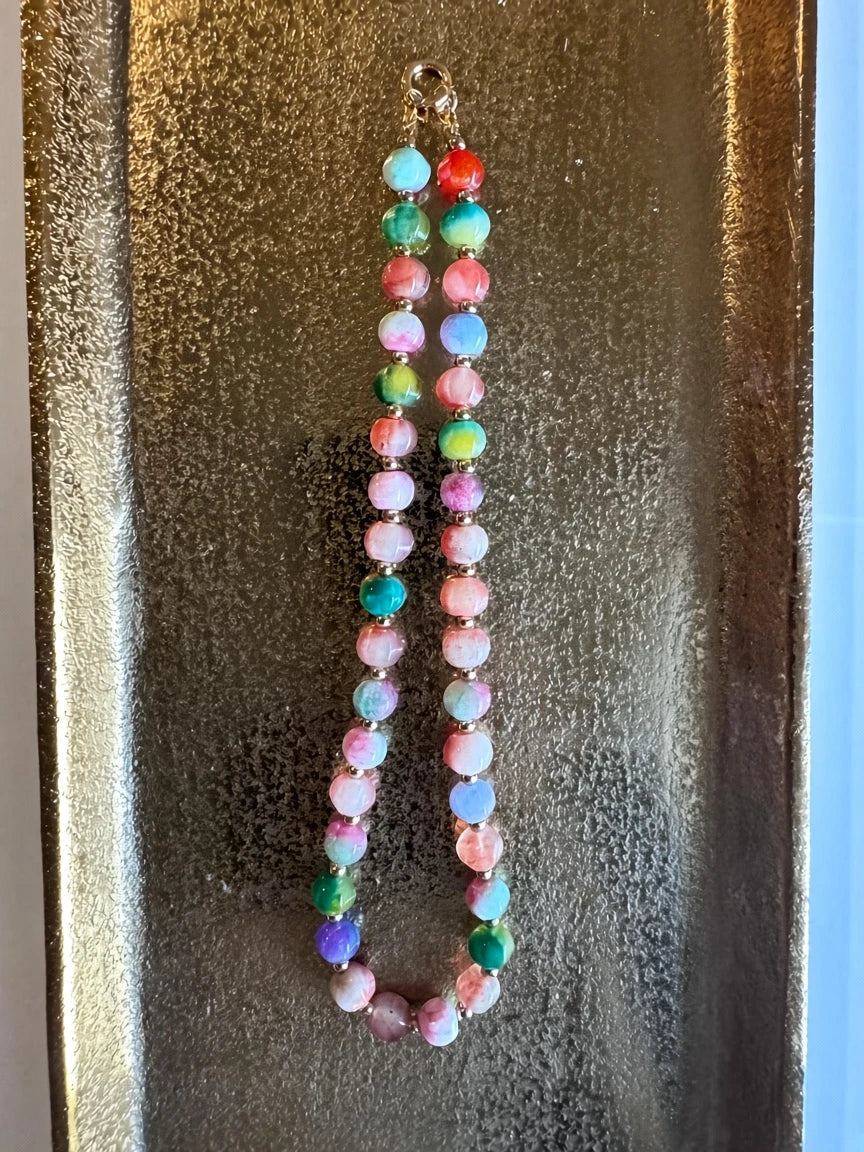 Hue La La Gems multi-colored gemstone beaded necklace with gold-tone spacers on a textured gold display tray