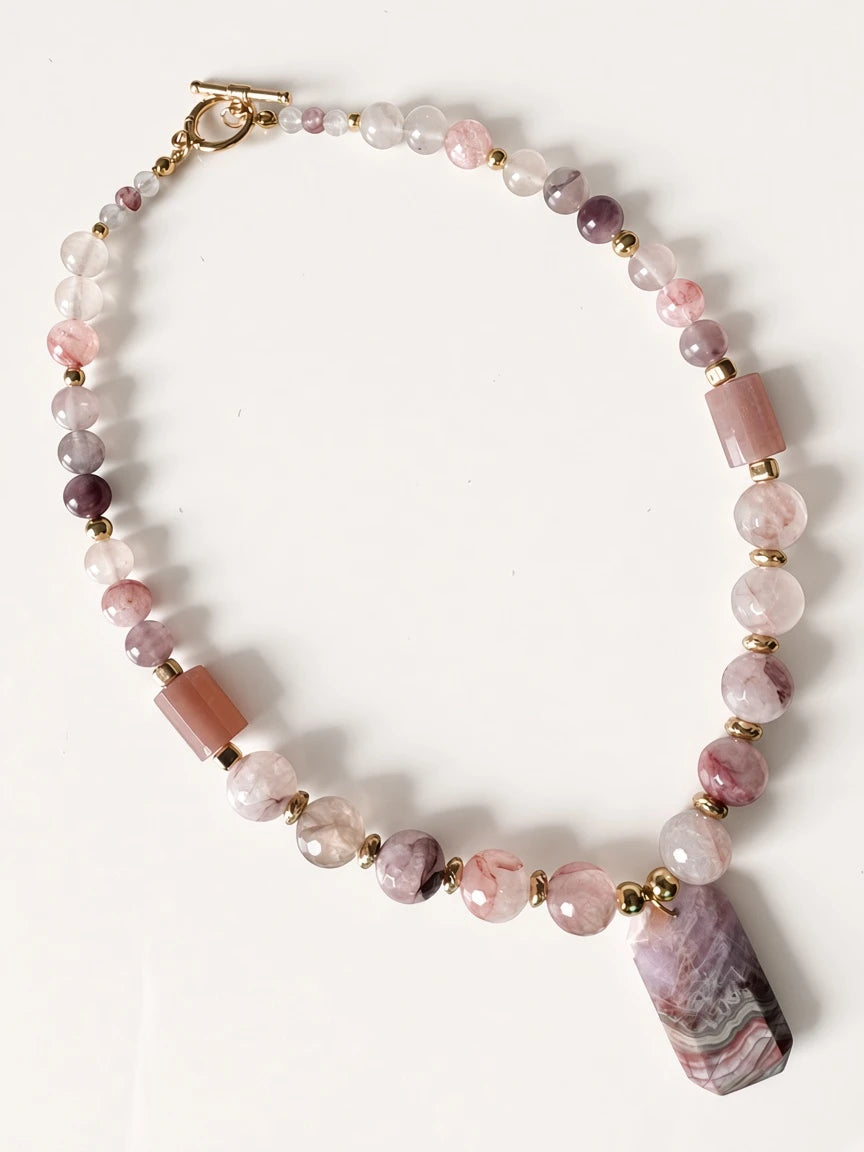Hue La La Gems beaded statement necklace featuring pink and mauve gemstones with a geometric pendant and gold clasp.