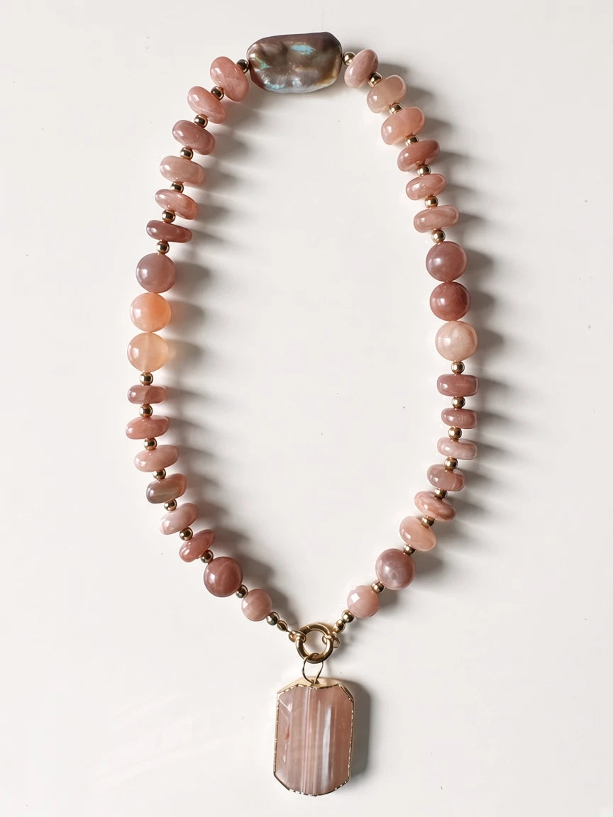 Hue La La Gems statement necklace featuring peach sunstone beads, a baroque pearl, and a gold-framed stone pendant.
