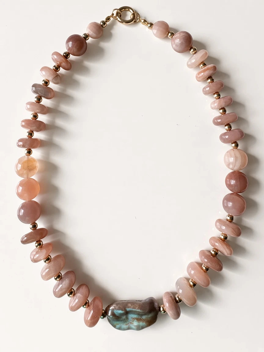 Hue La La Gems statement necklace featuring peach sunstone beads, gold spacers, and a central iridescent baroque pearl.